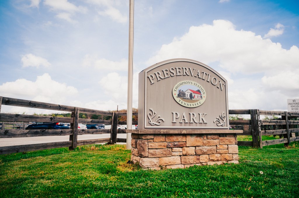 A stone sign for Thompson's Station Preservation Park stands in a grassy area beside a wooden fence in Williamson County, Tennessee.