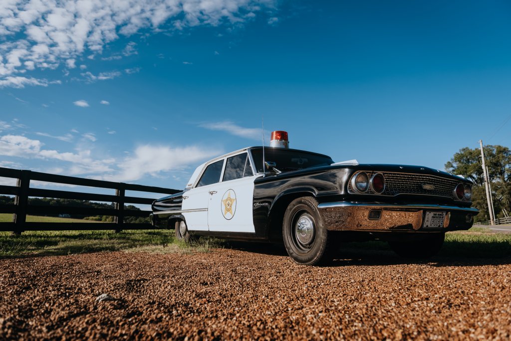 A vintage black and white police cruiser parked on gravel near a wooden fence in Williamson County, Tennessee.