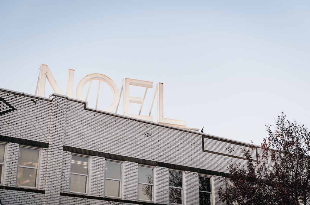 A large, illuminated 'NOEL' sign adorns the roof of a white brick building at dusk in Williamson County, Tennessee.