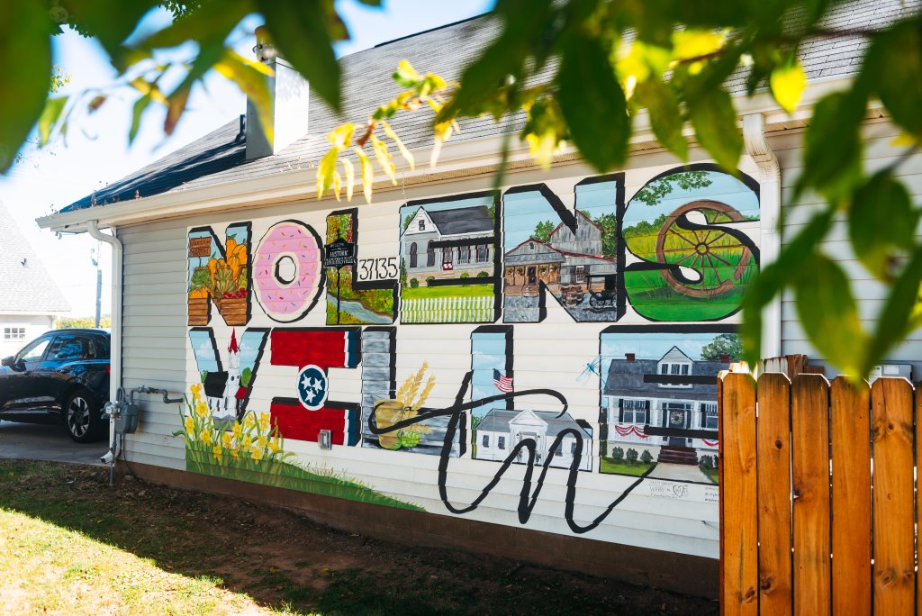 A vibrant mural spells out 'NOLESENSVILLE, TN' with colorful letters showcasing local scenes, including a doughnut, a barn, and a house with a red roof in Williamson County, Tennessee.