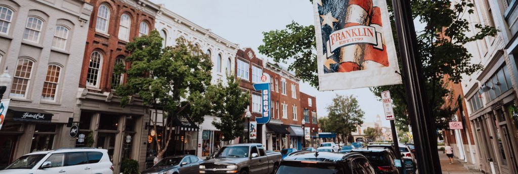 A bustling downtown street lined with colorful buildings and parked cars in Williamson County, Tennessee.