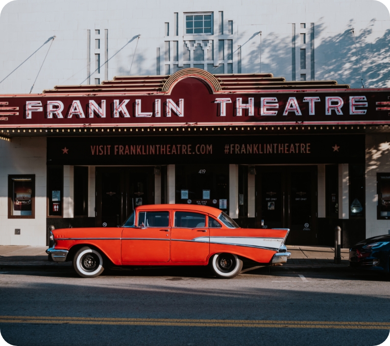A vibrant orange classic car is parked in front of the Franklin Theatre marquee in Williamson County, Tennessee.