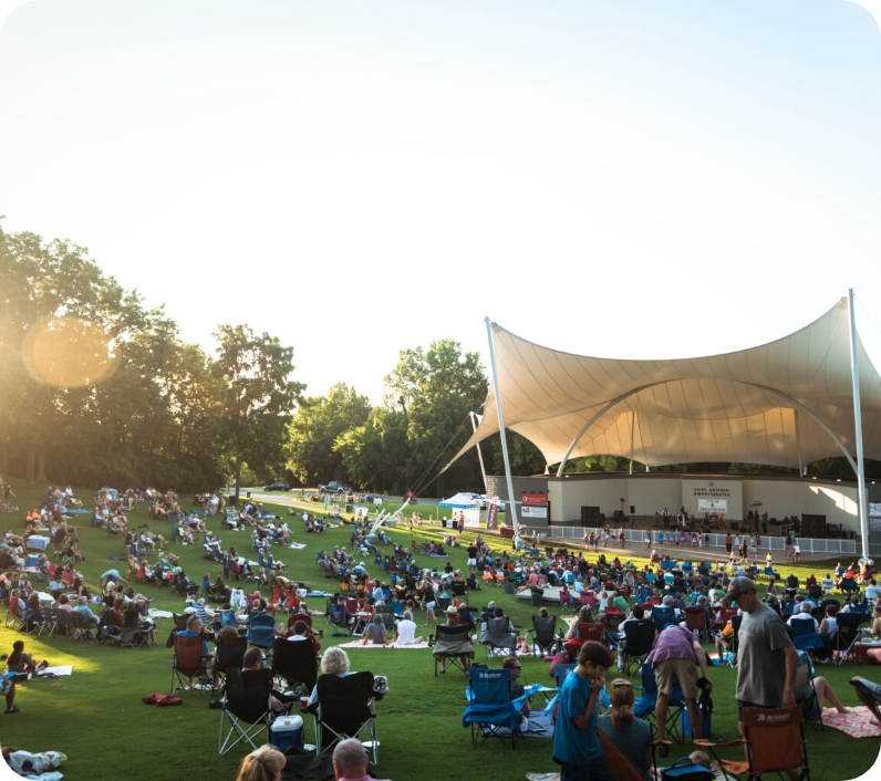A large crowd enjoys an outdoor concert under a curved white canopy in a grassy park in Williamson County, Tennessee.