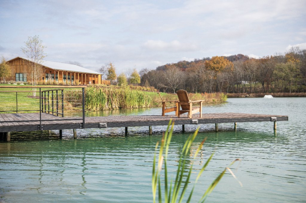 A serene lakeside scene with a wooden dock, Adirondack chair, and a rustic building in the background in Williamson County, Tennessee.