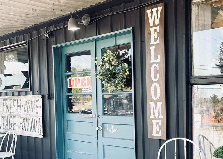 A charming blue door with a welcome sign and greenery greets visitors to a quaint shop in Williamson County, Tennessee.
