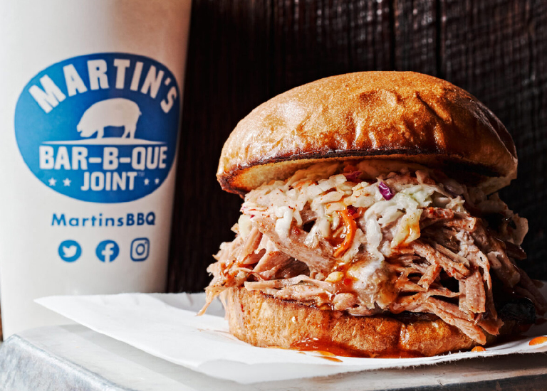 A mouthwatering pulled pork sandwich with coleslaw on a toasted bun, accompanied by a Martin's BBQ cup in Williamson County, Tennessee.