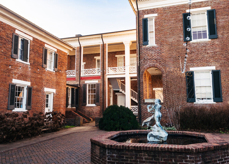 Spring Hill A courtyard with a brick fountain featuring a statue of a woman, surrounded by red brick buildings with white columns and shutters in Williamson County, Tennessee.