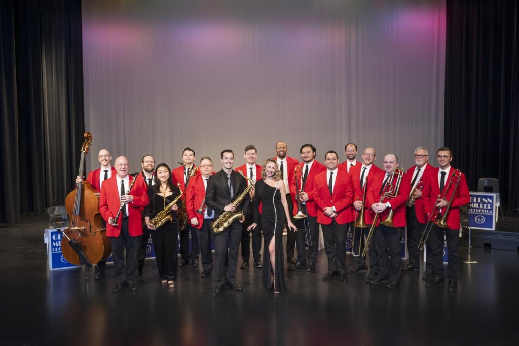 A jazz ensemble of 15 musicians in red suits and black ties pose on stage with their instruments in Williamson County, Tennessee.