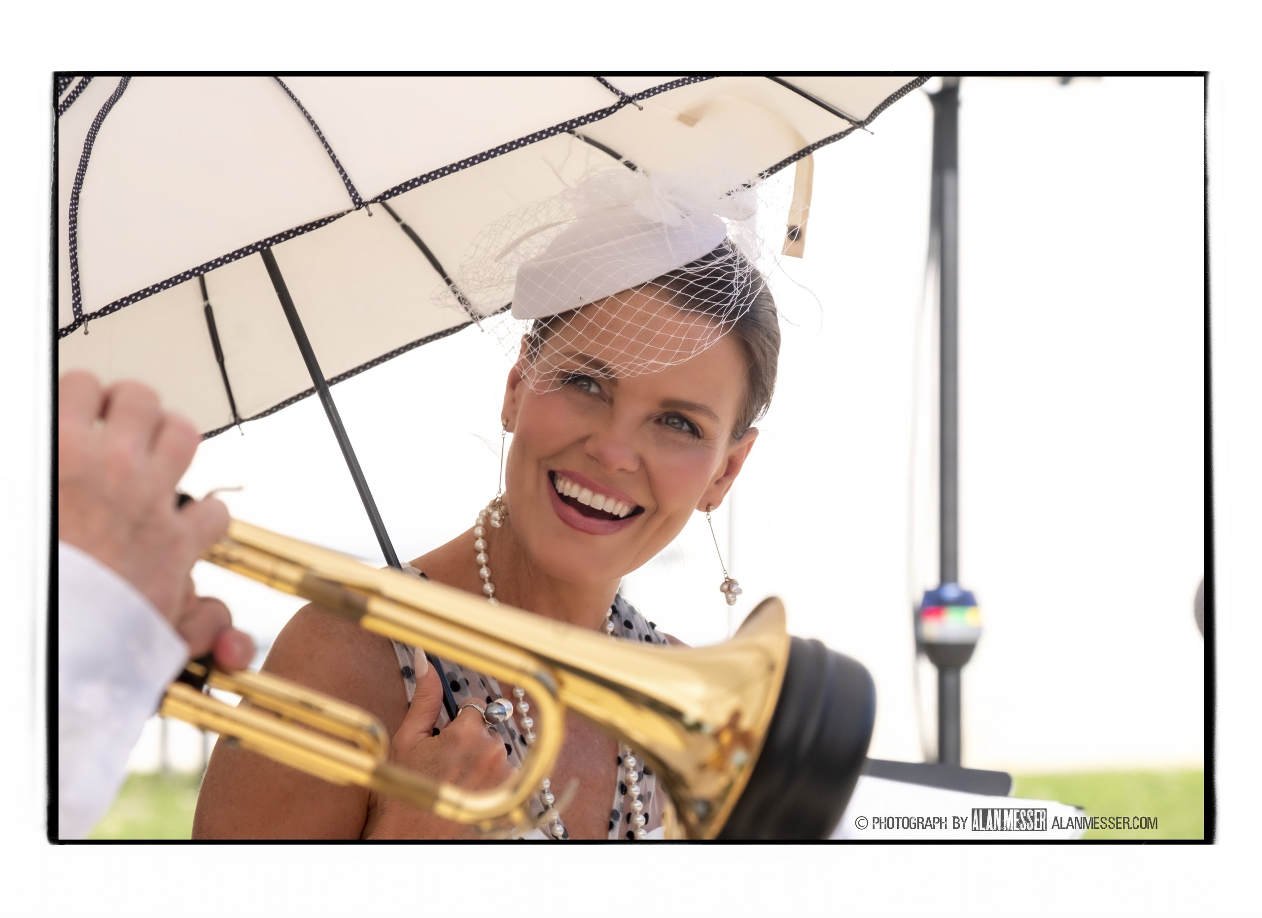 A woman in a polka-dot dress and hat holds a golden trumpet under a parasol in Williamson County, Tennessee.