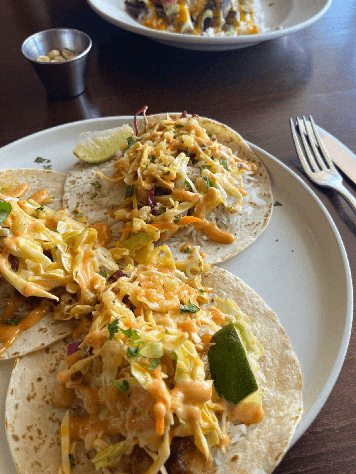 Three tacos with cabbage slaw, orange sauce, and lime wedges on a white plate in Williamson County, Tennessee.