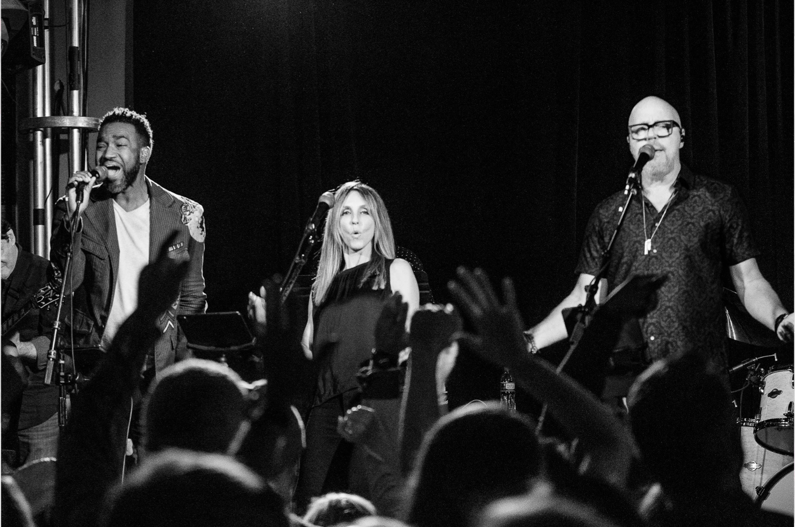 A black and white photograph of a band performing on stage with three members singing into microphones in Williamson County, Tennessee.
