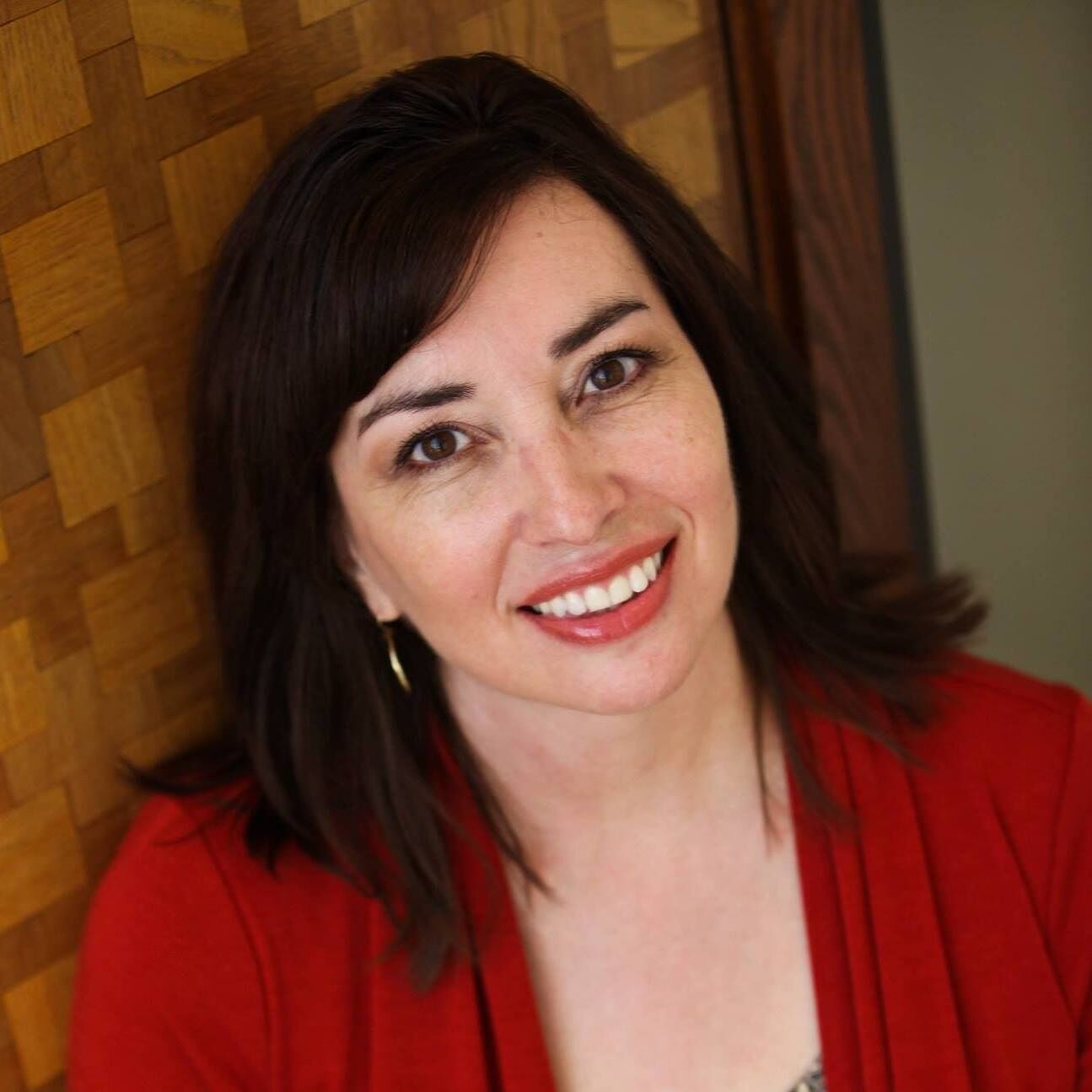 A smiling woman with dark hair wearing a red cardigan against a wooden background in Williamson County, Tennessee.