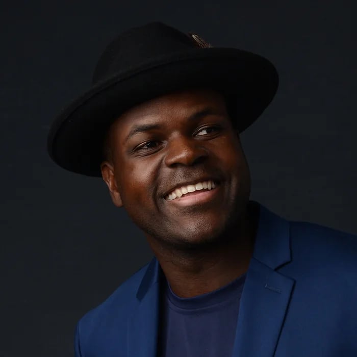 A smiling man wearing a black hat and blue suit jacket against a dark background in Williamson County, Tennessee.