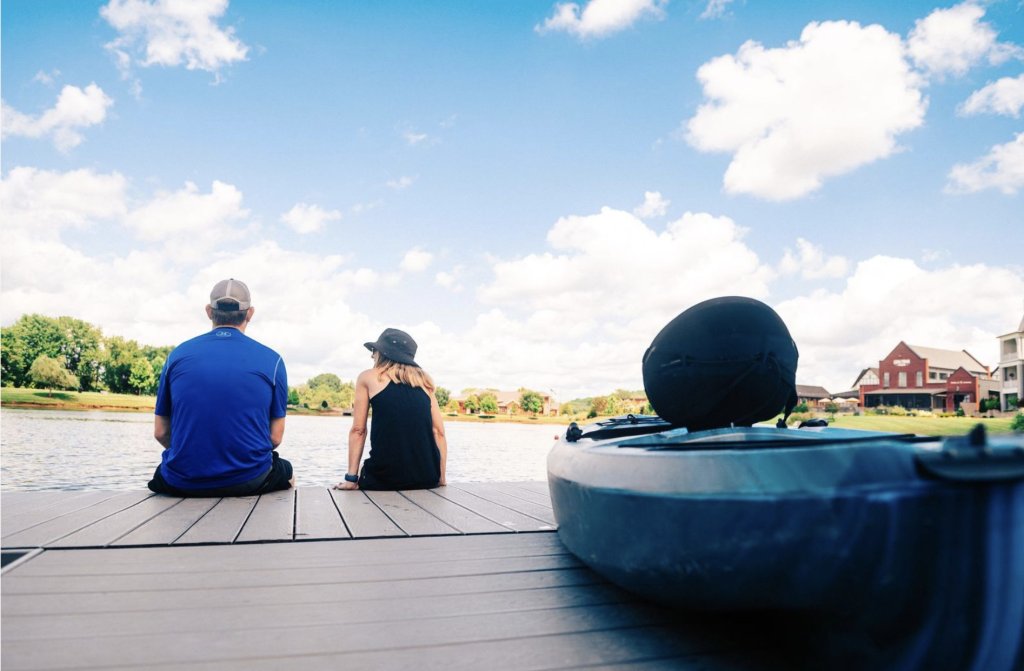 A couple sits on a wooden dock overlooking a serene lake with a kayak nearby in Williamson County, Tennessee.