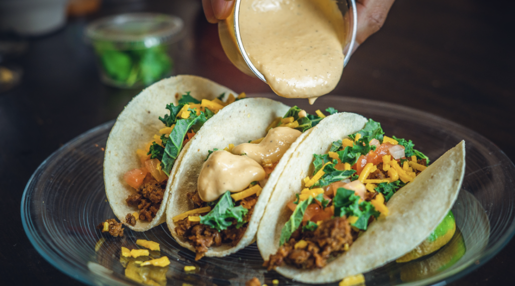 Taco ’Bout Tasty: 10 of Our Favorite Franklin Taco Joints A person is pouring creamy sauce over three colorful tacos on a glass plate in Williamson County, Tennessee.