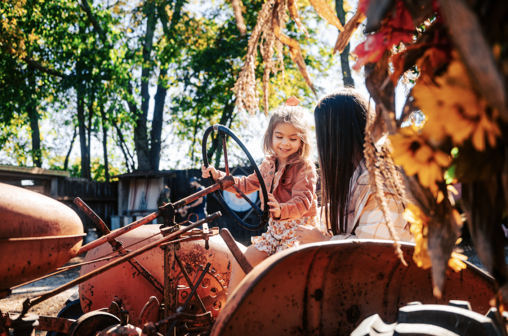 A young girl in a floral dress sits on an old tractor, smiling as she holds the steering wheel in Williamson County, Tennessee.