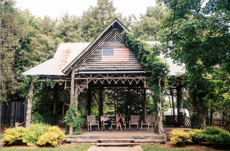 Rustic wooden gazebo with American flag, surrounded by lush greenery and two people sitting inside in Williamson County, Tennessee.