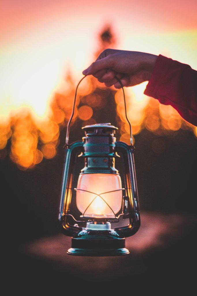 A hand holds a glowing lantern against a backdrop of a fiery sunset with silhouetted trees in Williamson County, Tennessee.