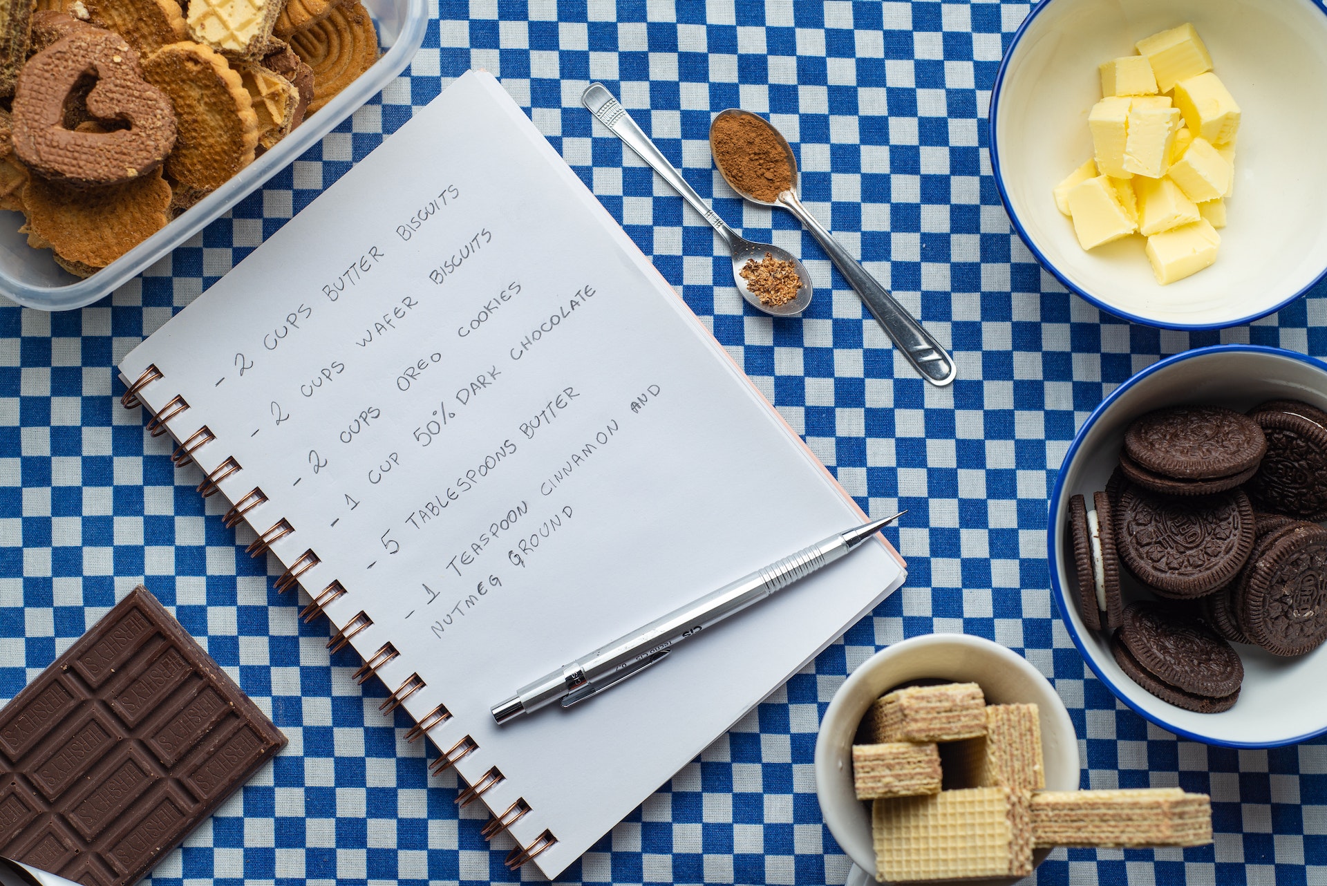 A recipe notebook with cookie ingredients and utensils on a blue checkered tablecloth in Williamson County, Tennessee.