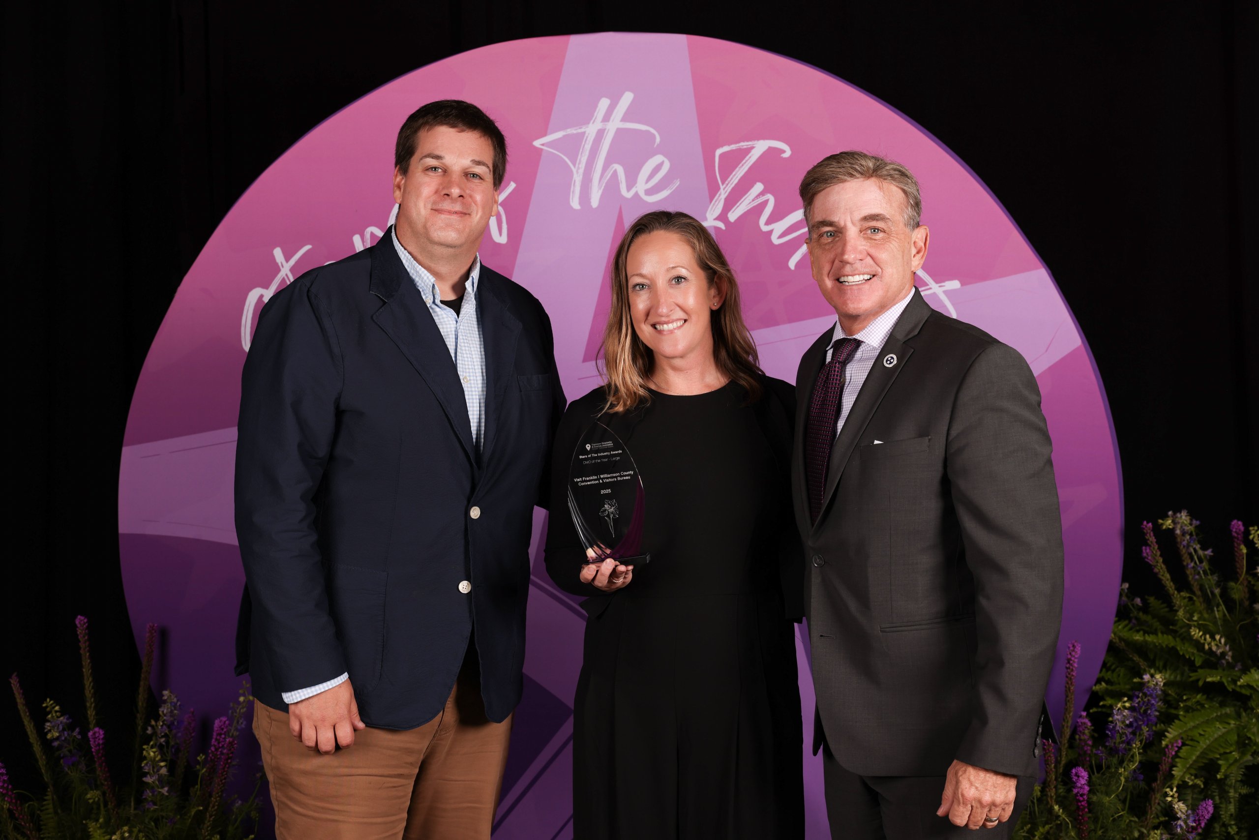 VISIT FRANKLIN NAMED DESTINATION MARKETING ORGANIZATION OF THE YEAR Three people in formal attire stand in front of a pink backdrop with an award in Williamson County, Tennessee.