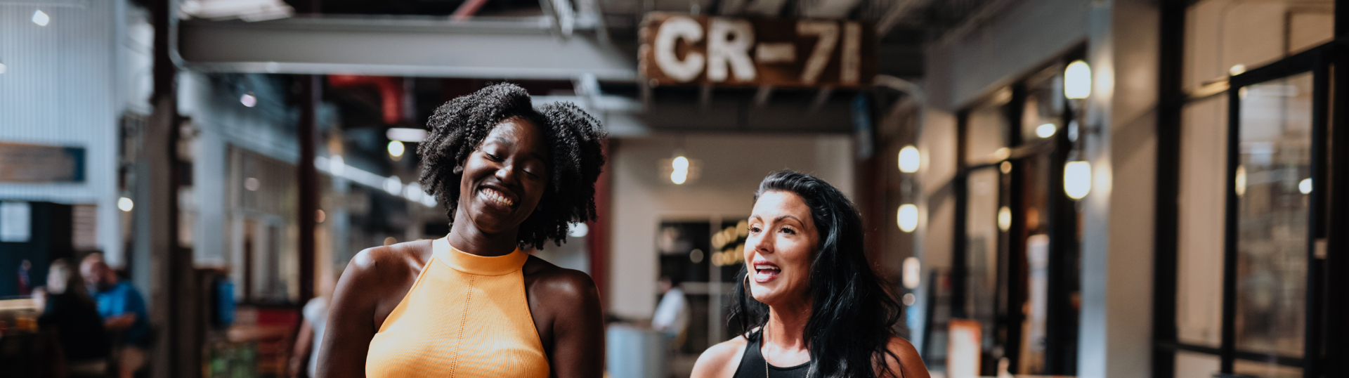 Two women with bright smiles walking together in a bustling indoor marketplace in Williamson County, Tennessee.