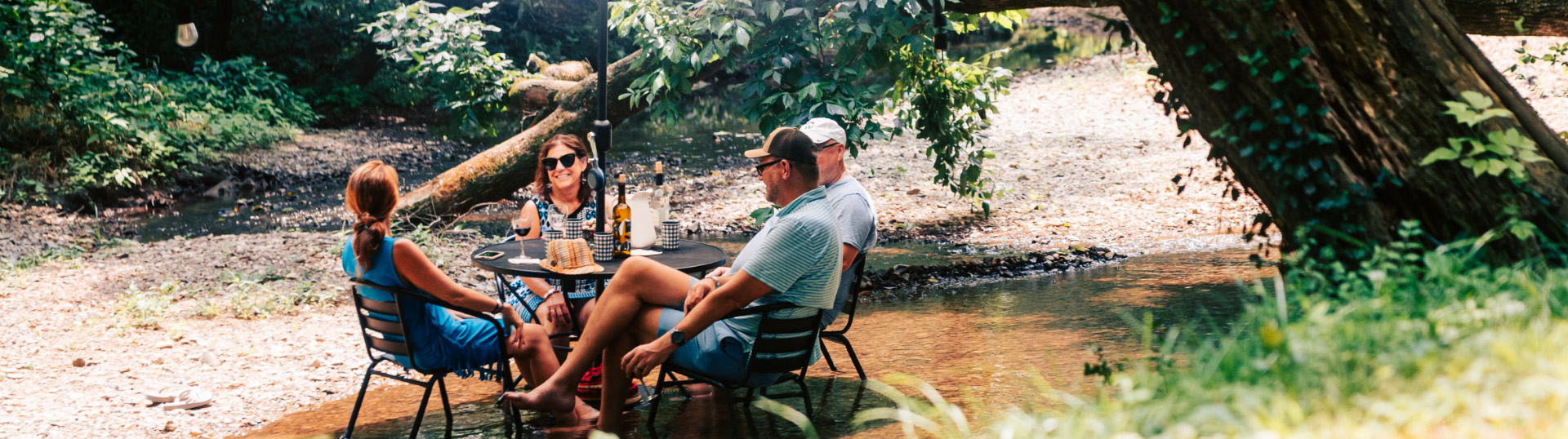 Four people enjoying a picnic by a stream in a wooded area in Williamson County, Tennessee.