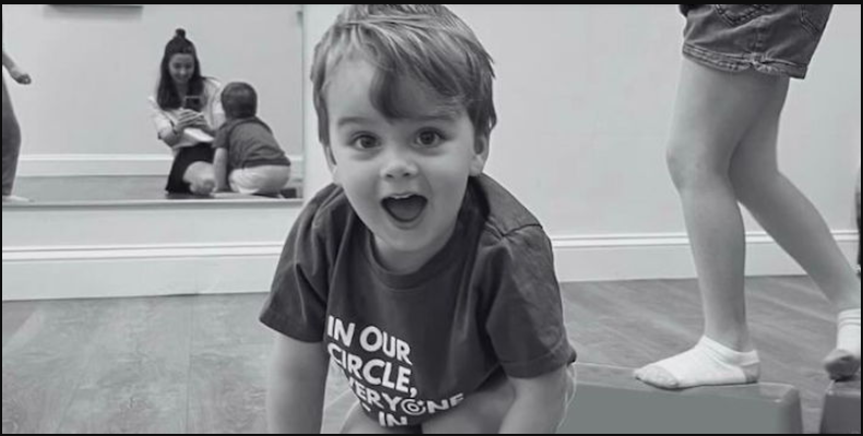 A young boy with short hair is kneeling on the floor, smiling broadly at the camera in Williamson County, Tennessee.