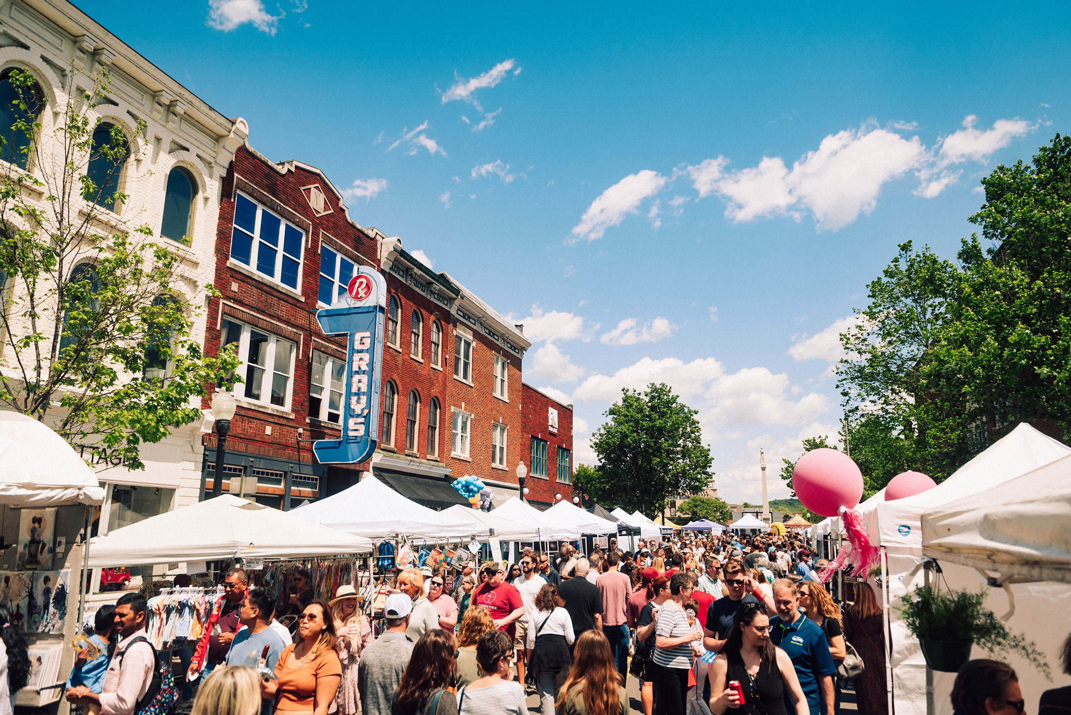 Crowded outdoor market with white tents, people shopping, and colorful balloons along a brick street in Williamson County, Tennessee.