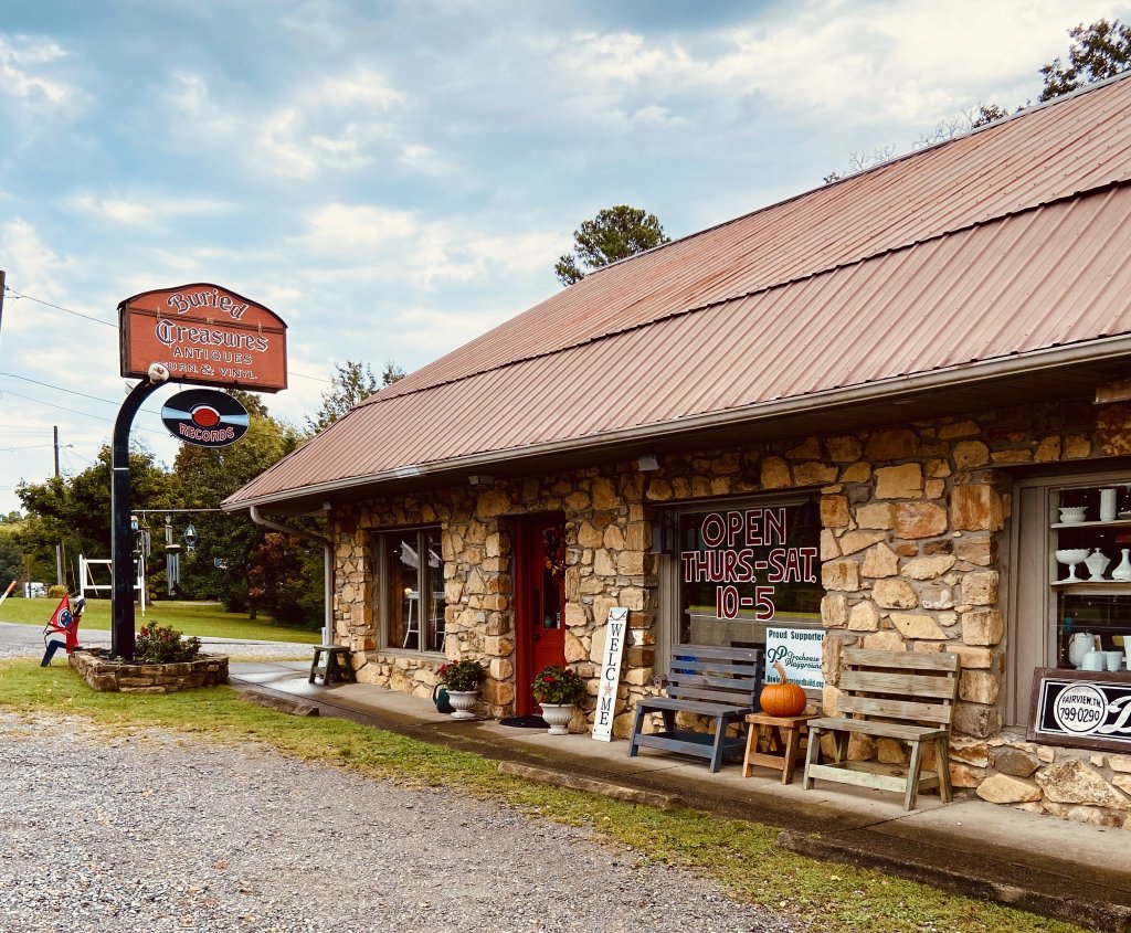 A quaint stone building with a red roof and wooden benches outside, featuring a sign for 'Buried Treasures Antiques' in Williamson County, Tennessee.