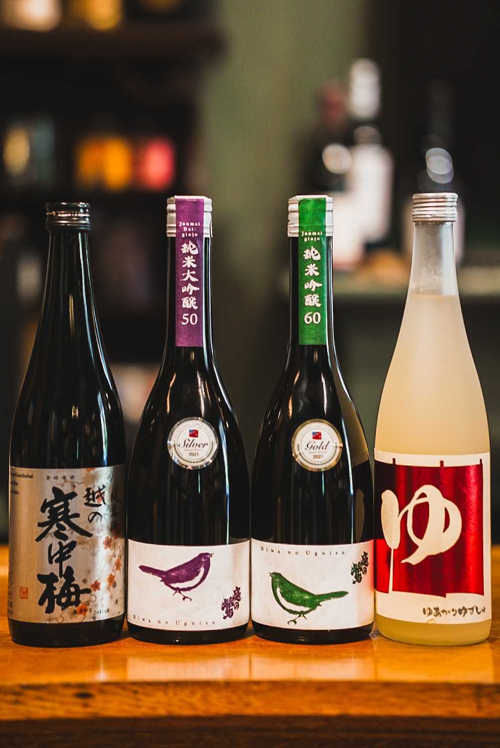 Sake Tasting at Saint Goose! Four bottles of Japanese sake with colorful labels featuring birds and Asian characters in Williamson County, Tennessee.