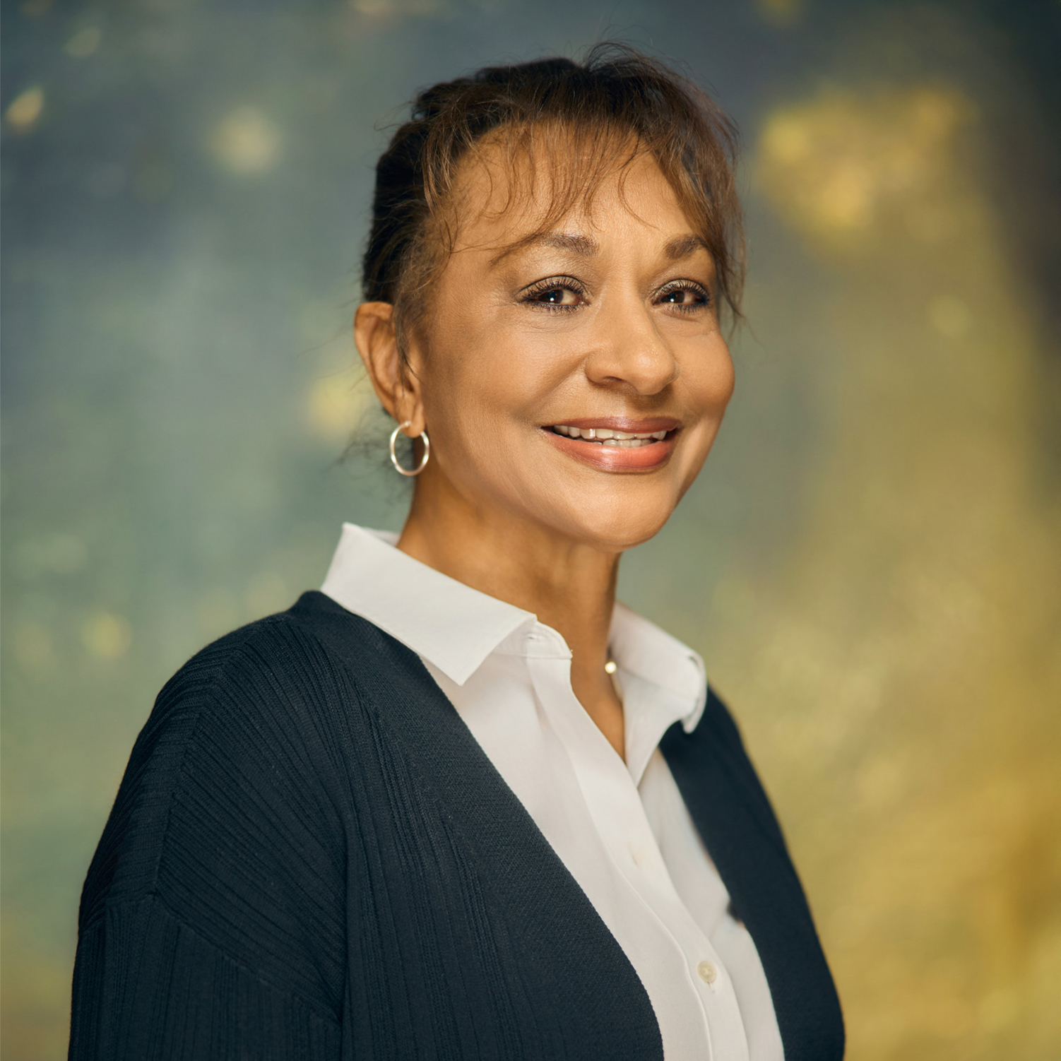 Meet The Team A smiling woman with hoop earrings wearing a dark cardigan over a white shirt in Williamson County, Tennessee.