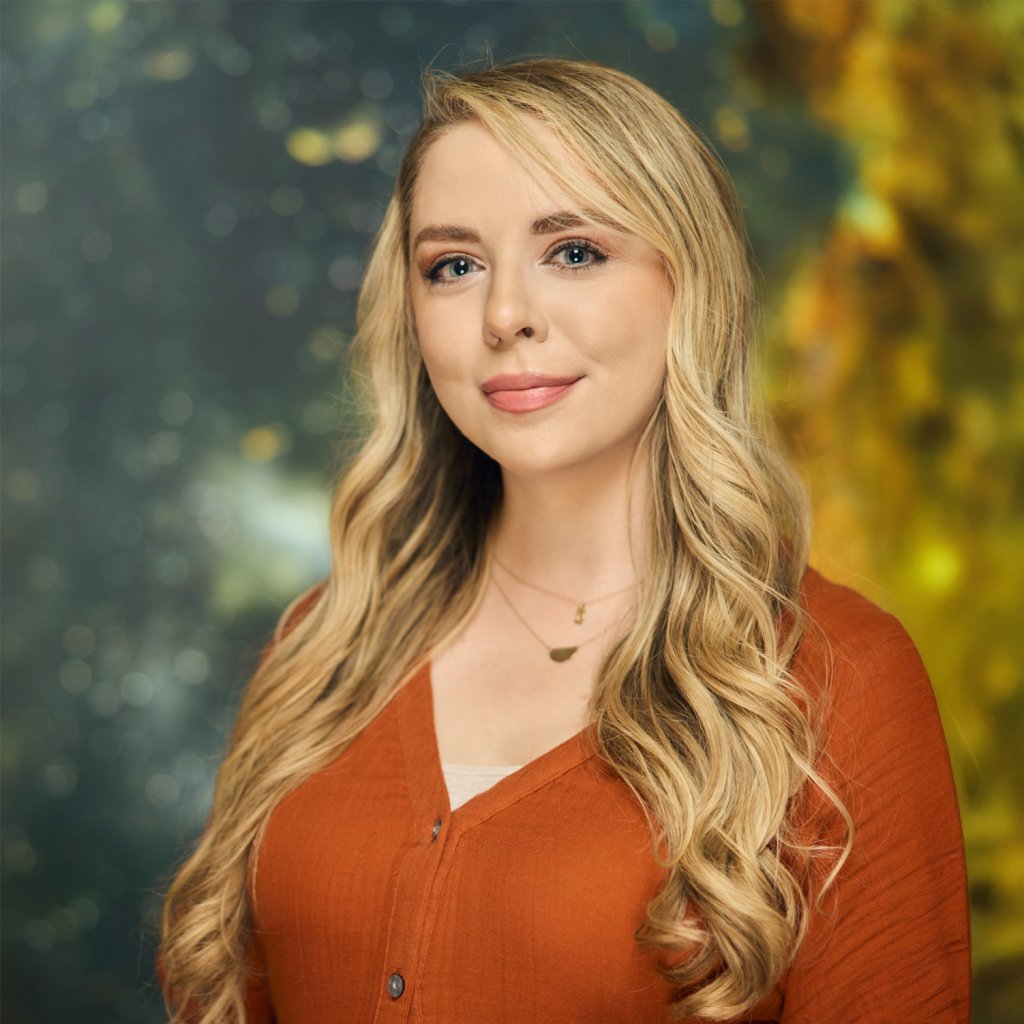 A woman with long blonde hair smiles wearing an orange shirt against a galaxy-themed background in Williamson County, Tennessee.