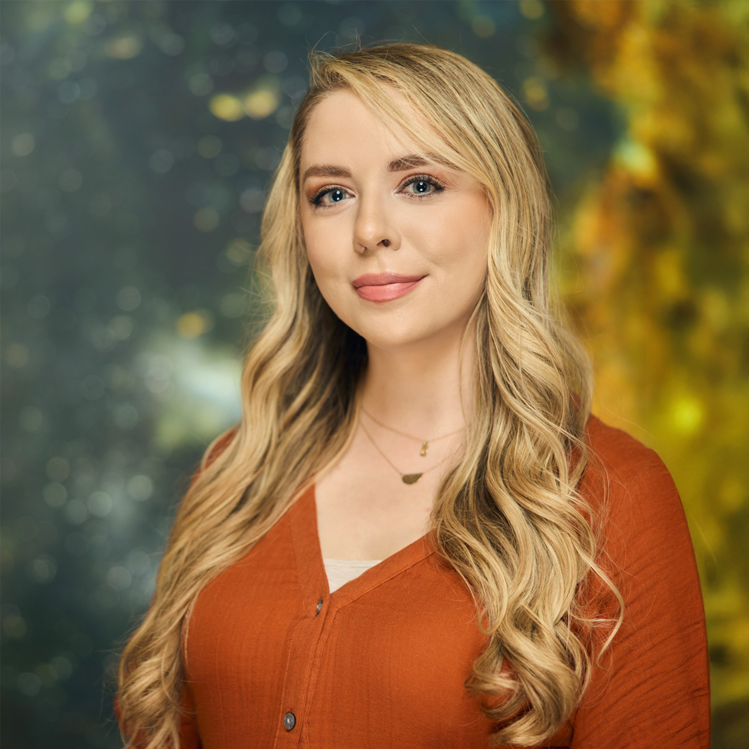 Meet The Team A woman with long blonde hair smiles wearing an orange shirt against a galaxy-themed background in Williamson County, Tennessee.