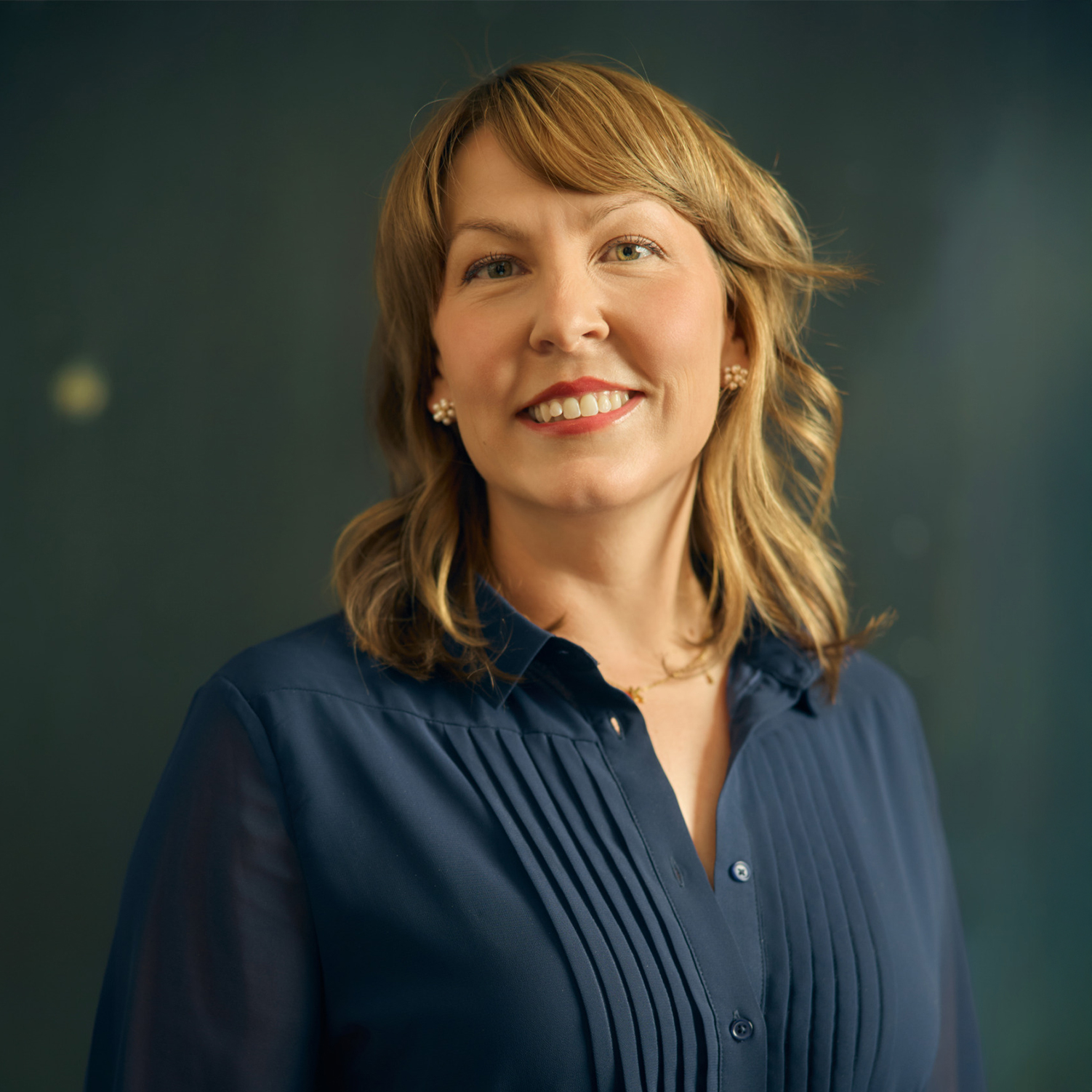 Meet The Team A smiling woman with blonde hair wearing a navy blue blouse with pleats in Williamson County, Tennessee.