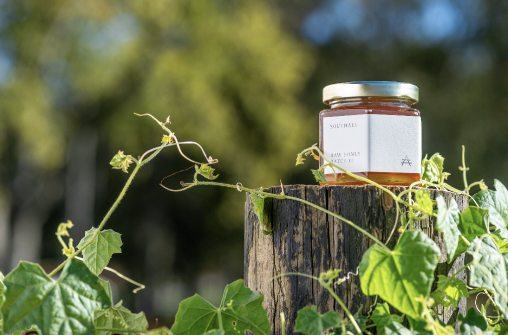A jar of raw honey sits on a wooden post surrounded by green leaves in Williamson County, Tennessee.
