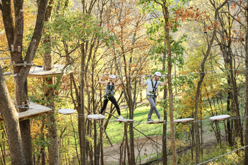 Two people ziplining through a colorful autumn forest, wearing helmets and harnesses in Williamson County, Tennessee.