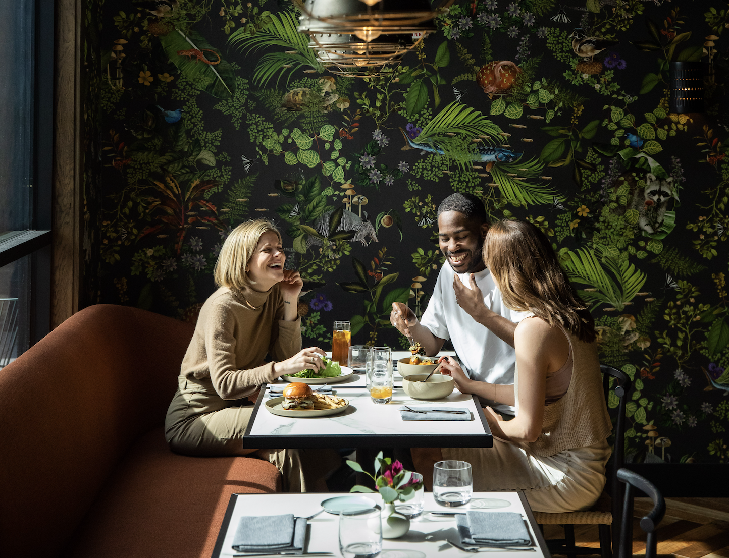 Three friends enjoy a meal together at a restaurant with a vibrant floral wallpaper backdrop in Williamson County, Tennessee.
