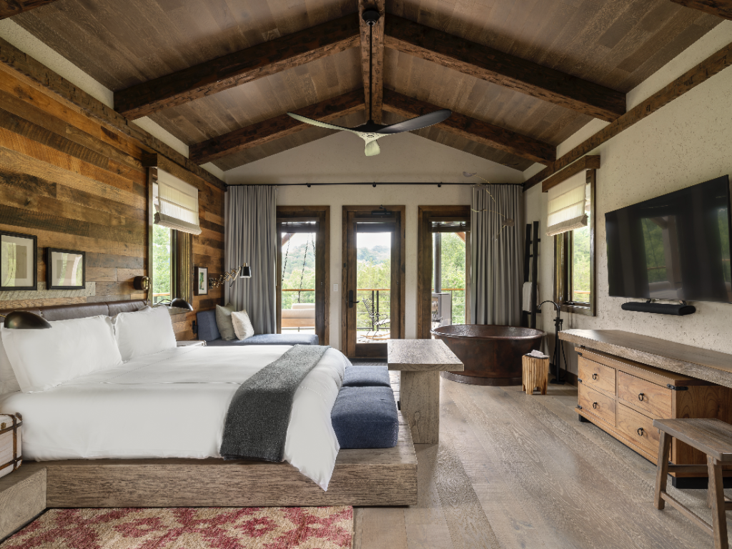 A rustic, modern bedroom with a wooden bed, exposed beams, and a large window overlooking nature in Williamson County, Tennessee.