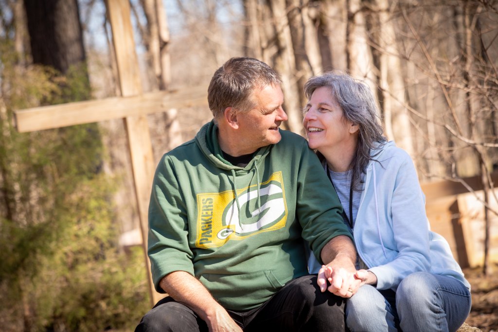 A couple sits close together in a wooded area, smiling and holding hands in Williamson County, Tennessee.