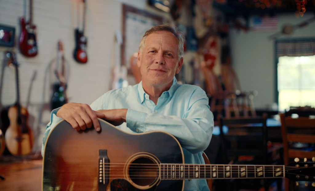 Leiper's Fork, Tennessee: The Revival of a Small-Town Gem A man in a light blue shirt holds an acoustic guitar in a room filled with various musical instruments in Williamson County, Tennessee.