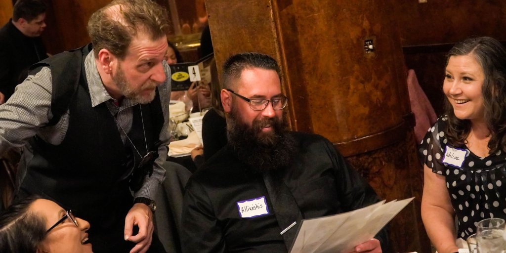 A group of people are gathered around a table, laughing and reading menus at a formal event in Williamson County, Tennessee.