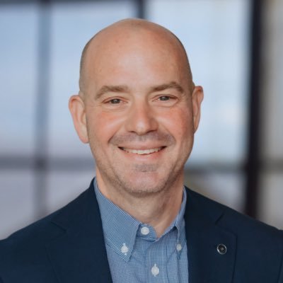 Joel J. Miller A smiling bald man in a navy blue suit and blue checkered shirt in Williamson County, Tennessee.