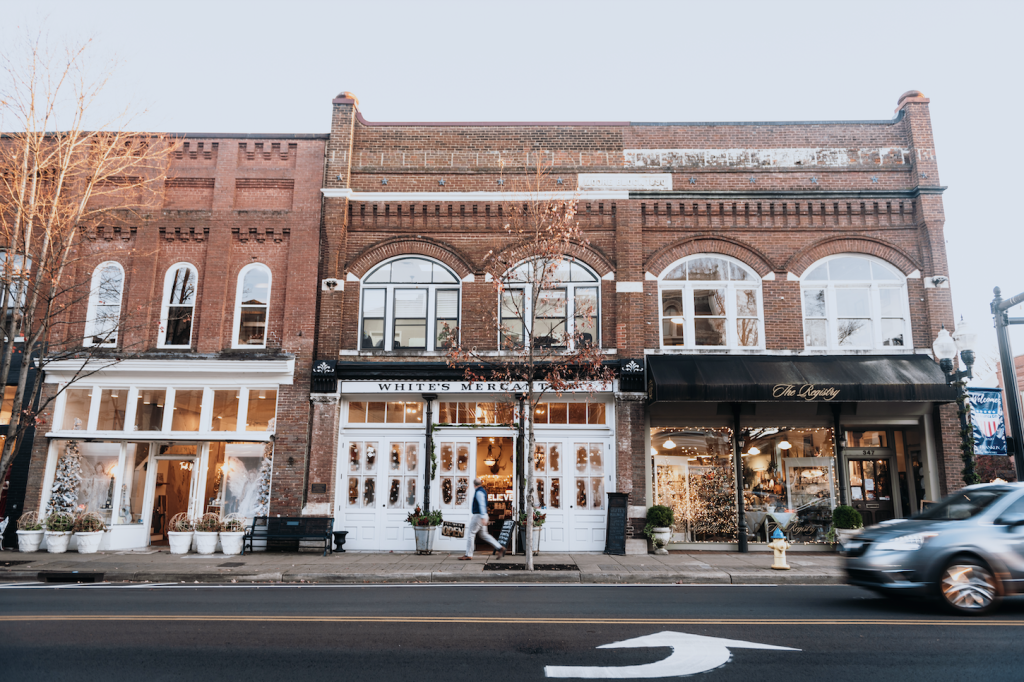 Three-story brick buildings line a street with storefronts, windows, and a moving car in Williamson County, Tennessee.