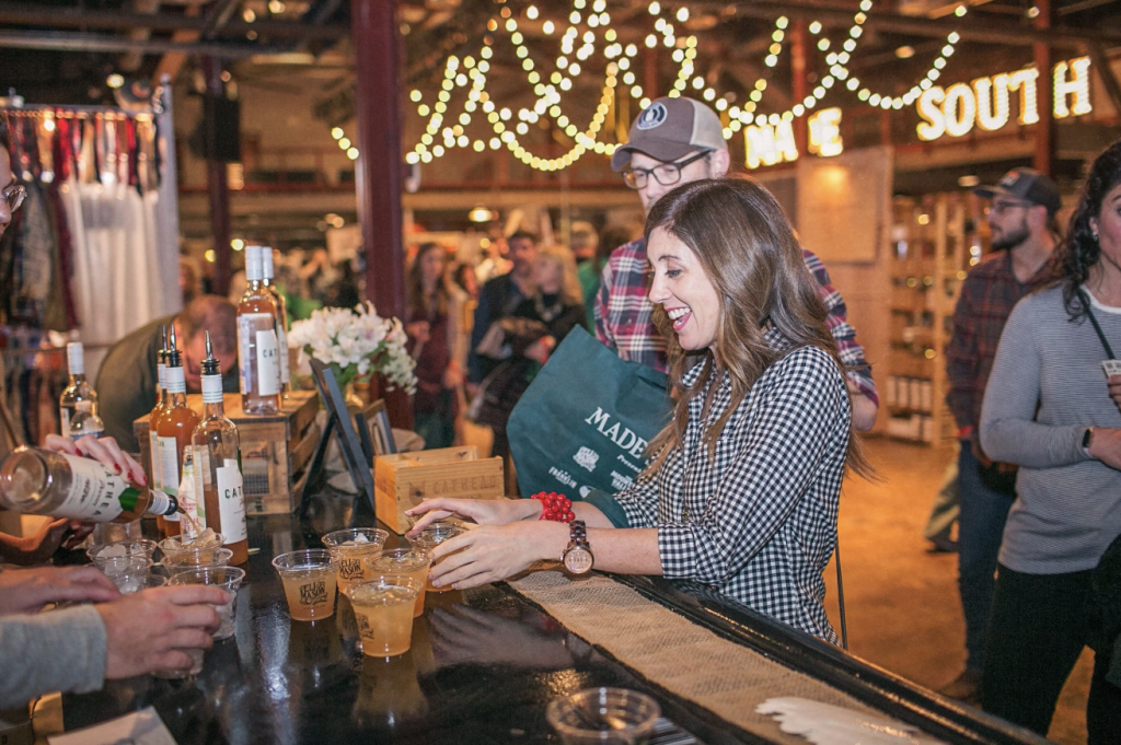 A woman in a checkered shirt pours drinks at a crowded bar with hanging lights in Williamson County, Tennessee.