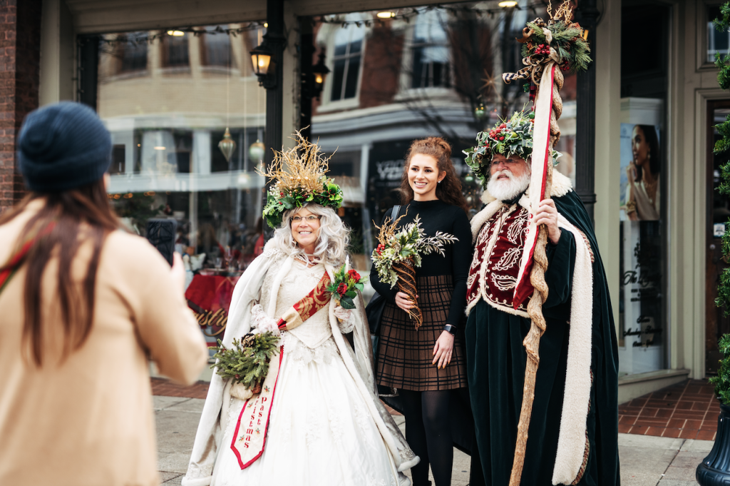 Three people dressed in elaborate costumes with floral crowns and staffs pose for a photo in Williamson County, Tennessee.