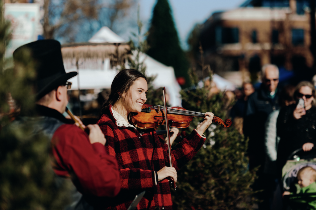 A woman in a red and black plaid shirt plays the violin while a man in a top hat accompanies her on a flute in Williamson County, Tennessee.