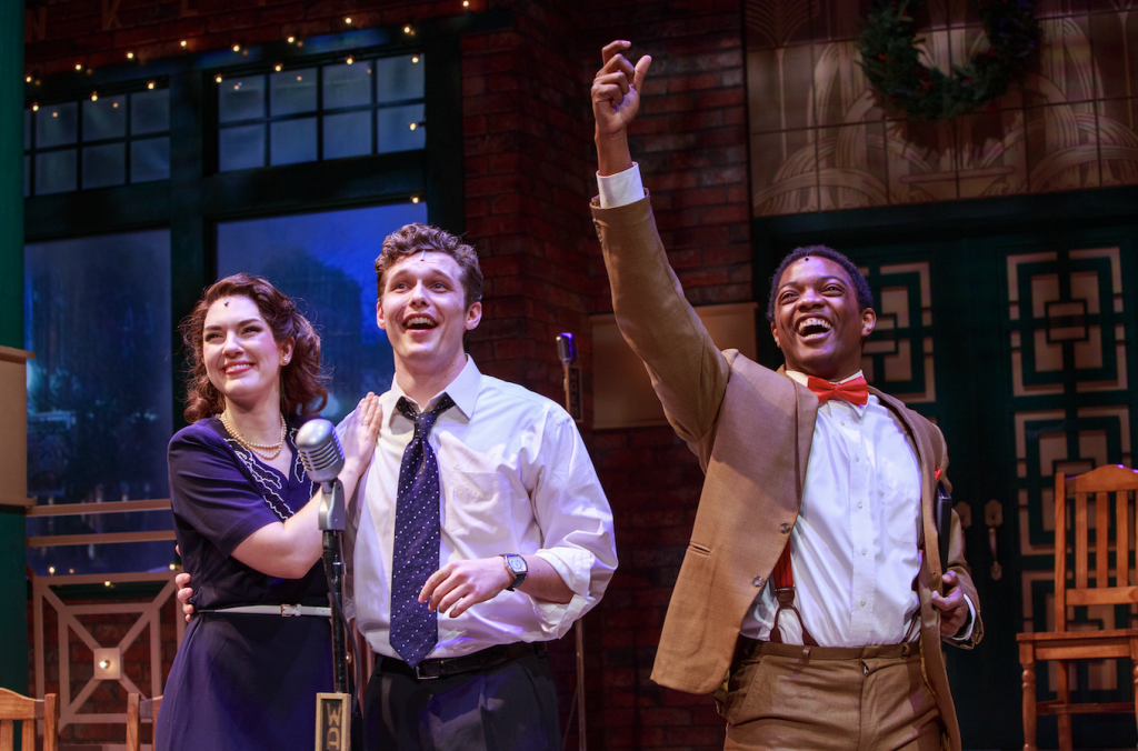 Three performers celebrate on stage, with a man in a brown suit raising his arm in triumph in Williamson County, Tennessee.