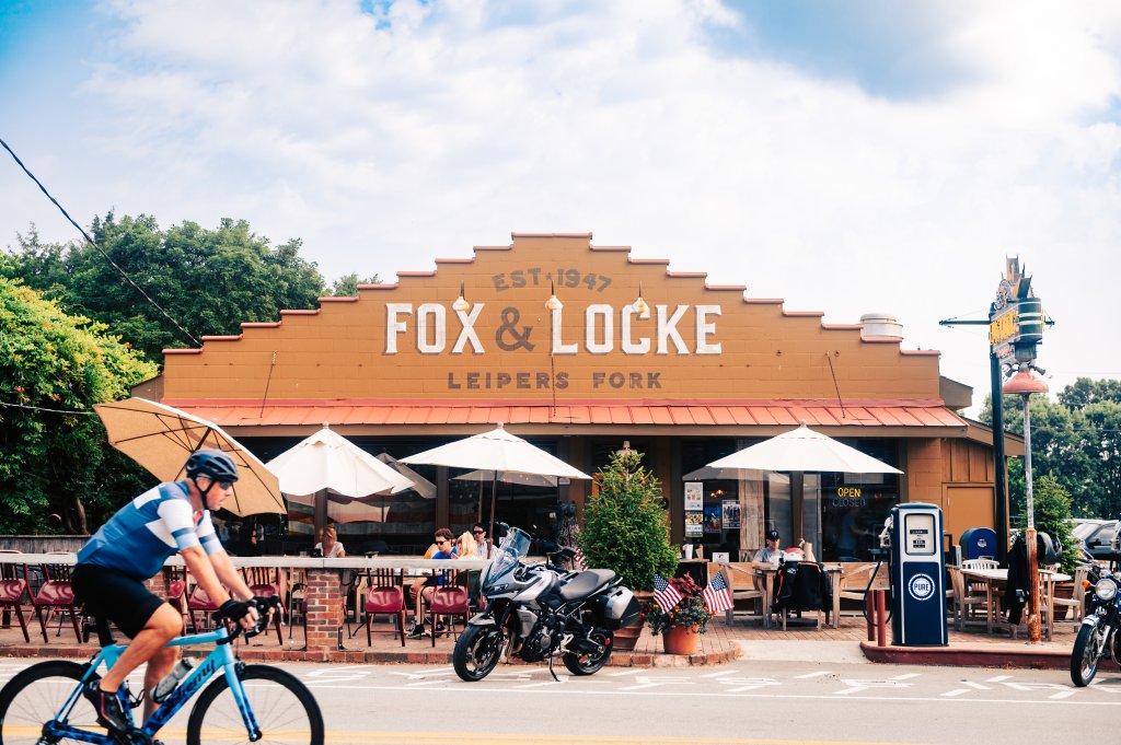 A cyclist rides past a restaurant with outdoor seating and a vintage gas pump in Williamson County, Tennessee.