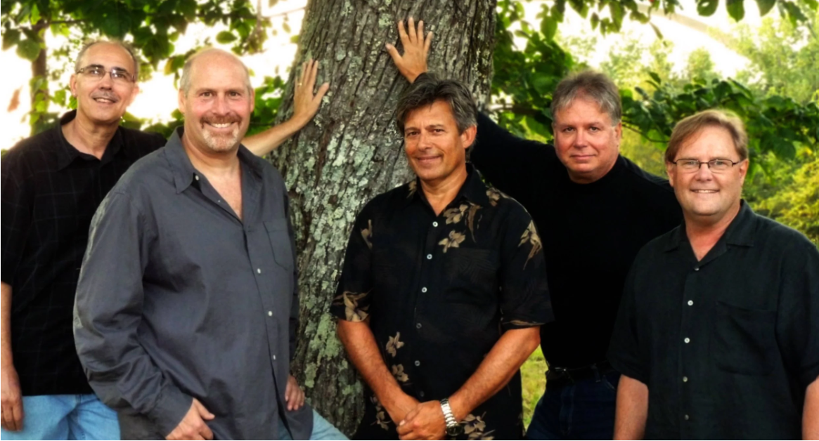 Five smiling men pose together outdoors, leaning against a large tree trunk in Williamson County, Tennessee.