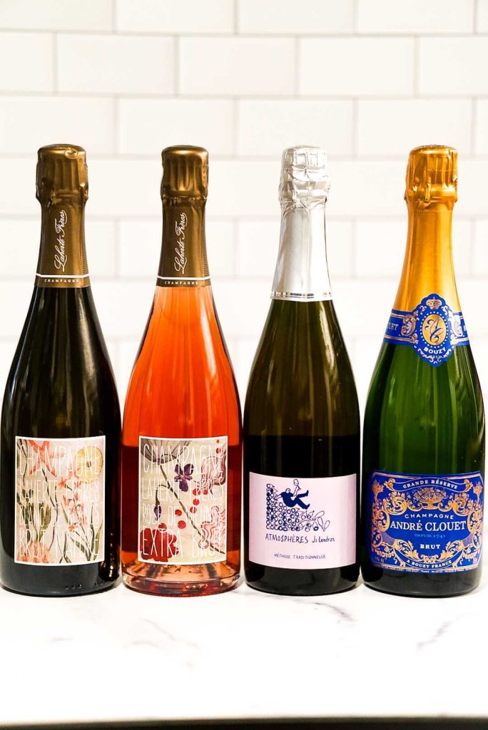 Holiday Bubbles & Cheers: Sparkling Wine Class at Saint Goose Four elegant champagne bottles with colorful labels stand side by side on a white surface in Williamson County, Tennessee.